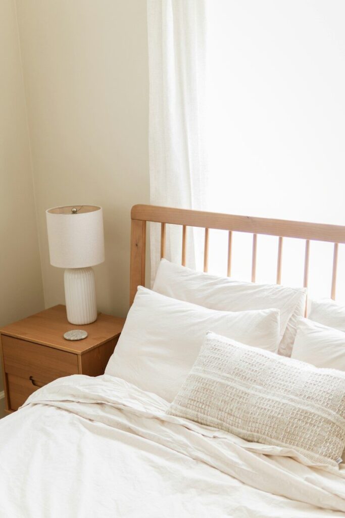A bright bedroom with white bedding, wooden headboard, and nightstand