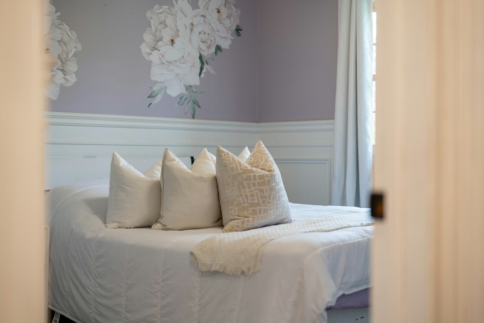 A bed with white pillows and floral wallpaper
